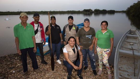 Das Bild zeigt mehrere Menschen, die am Ufer eines Flusses stehen