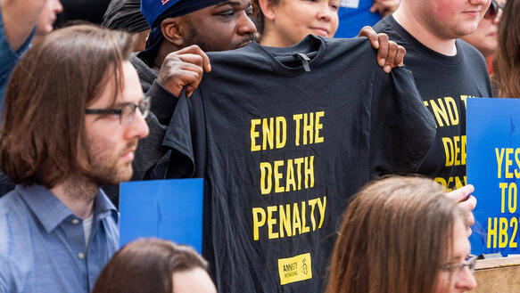 Das Bild zeigt viele Menschen, ein Mann hält dabei ein T-Shirt mit der Aufschrift "End the Death Penalty" in den Händen