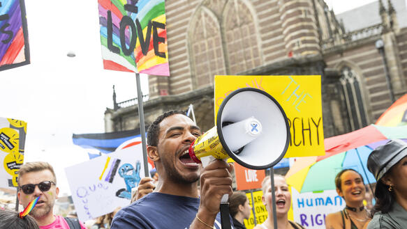 Das Bild zeigt das Porträtbild einer Person mit Megafon auf einer Demonstration