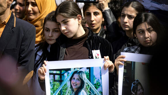 Das Foto zeigt trauernde Frauen und Mädchen bei einer Demonstration, die Porträtfotos von Mädchen und jungen Frauen in den Händen halten.