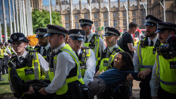 Mehrere uniformierte Polizisten tragen einen Demonstranten weg.