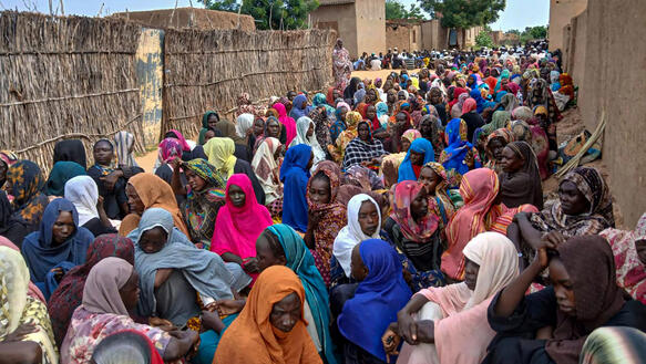 Dutzende Menschen sitzen auf dem Boden, sie schauen müde. 