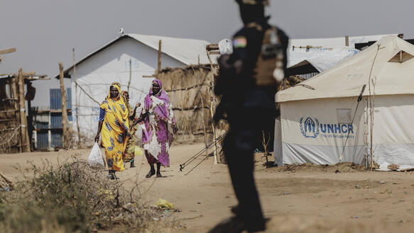 Im Vordergrund ein Soldat mit Gewehr, im Hintergrund mehrere Frauen
