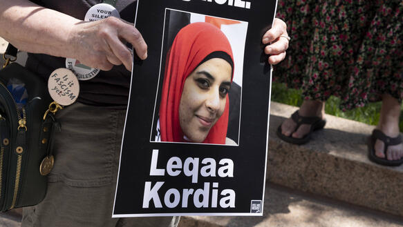 Das Foto zeigt eine Demonstrantin, die ein Pappschild in der Hand hält mit dem Foto von Leqaa Kordia, die auf dem Bild ein Kopftuch trägt.