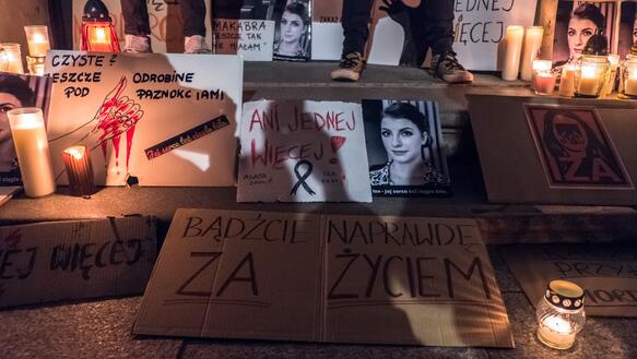 Das Foto zeigt Kerzen und Karten auf Treppenstufen vor einem Gebäude mit Fotos von einer jungen Frau.