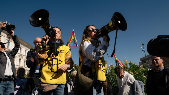 Das Foto zeigt zwei Frauen mit Megafonen bei einer Demonstration. Die tragen Leibchen mit Amnesty-Logo.