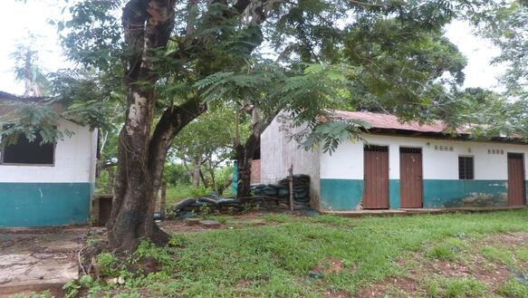 Das Foto zeigt zwei einstöckige Gebäude mit geschlossenen Metalltüren. Neben dem rechten Gebäude liegen mehrere Säcke. Zwischen den beiden Gebäuden steht ein Baum.