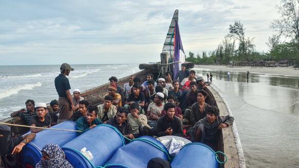 Rohingya auf einem Boot, das auf einen Sandstrand zuhält.
