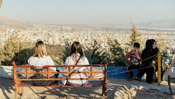 Frauen sitzen auf einer Bank auf einer Anhöhe, vor ihnen im Tal erstreckt sich Teheran.