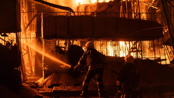 Das Foto zeigt einen Feuerwehrmann mit Wasserschlauch vor einem Gebäude, das lichterloh in Flammen steht.