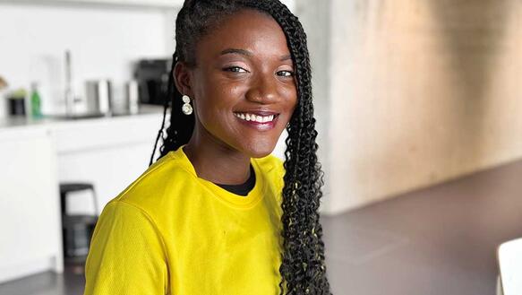 Eine junge Frau aus Ghana sitzt in einem Raum und lächelt.
