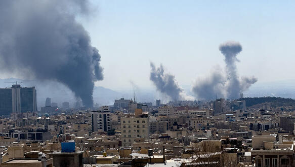 Drei große Rauchschwaden steigen in einer Stadt auf hoch in den Himmel.