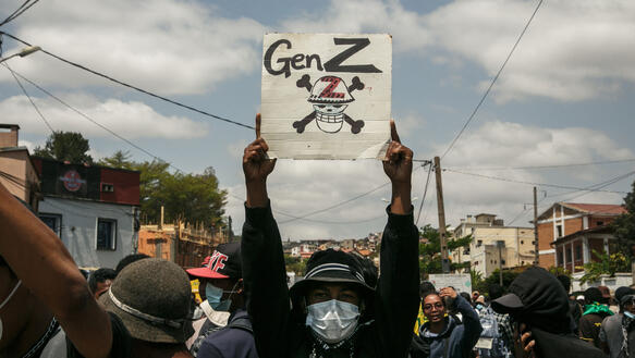Eine Person mit Mundschutz hält bei einer Demonstration ein Plakat hoch, auf dem ein Totenschädel mit Knochen abgebildet ist. Darüber steht: "Gen Z".