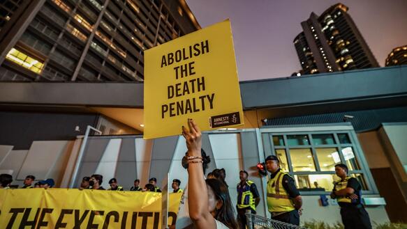Mehrere Personen mit Banner und Plakaten demonstrieren vor einem Gebäude. Auf dem Plakat im Vordergrund steht: "Abolish the Death Penalty".