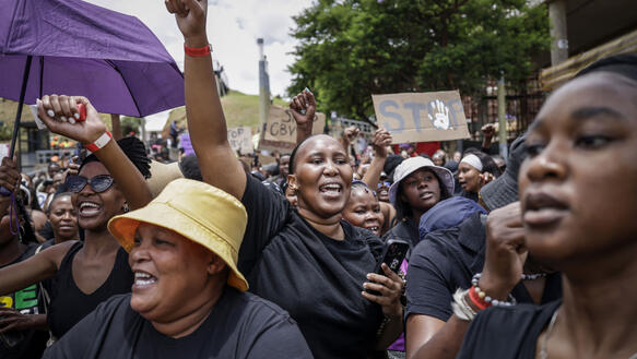 Das Foto zeigt demonstrierende Frauen. Eine Frau reckt ihre rechte Faust hoch in die Luft.