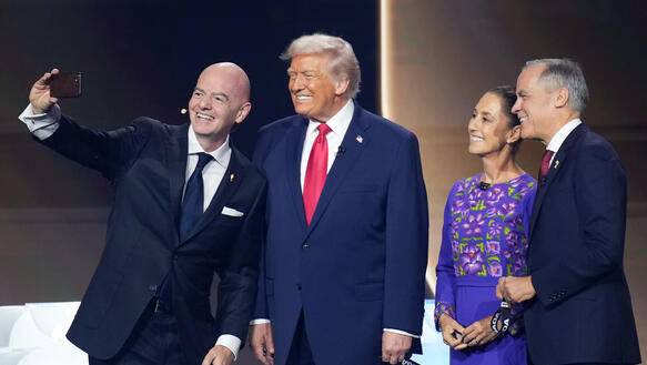 Gianni Infantino nimmt auf einer Bühne ein Selfie mit Donald Trump auf. Sie lächelnd. Neben ihn steht noch eine Frau und ein Mann, die ebenfalls in die Handykamera lächeln.