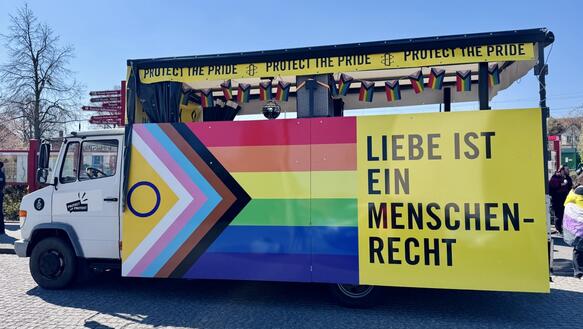 Foto von einem LKW mit einer seitlich angebrachten Pride-Flagge und dem Slogan "Liebe ist ein Menschenrecht"