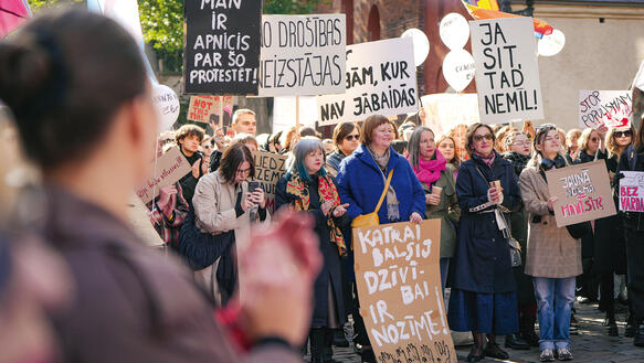 Menschen protestieren in Riga auf einer Straße, tragen viele selbstgemalte Shilder mit Parolen