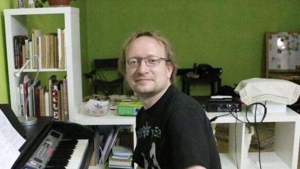 Mikhail Lochtchinin sitzt an einem Keyboad und lächelt in die Kamera. Er trägt eine Brille.