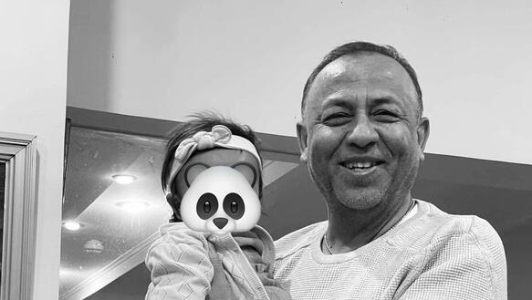 Das Foto zeigt Sylvain Rabetsaroana, der ein kleines Kind auf dem Arm trägt. Er lächelt in die Kamera. Das Foto wurde digital bearbeitet, um das Gesicht des Kindes unkenntlich zu machen. Auf dem Gesicht wurde ein Panda-Gesicht digital platziert.