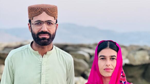 Das Foto zeigt Dad Shah und Fozia Baloc nebeneinander in einer Landschaft stehen und leicht in die Kamera lächelnd. Sie tragen traditionelle Kleidung.
