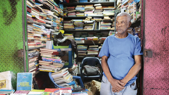 Ein Mann in seinen Siebzigern steht in der offenen stählernen Tür seines Buchladens in Caracas.