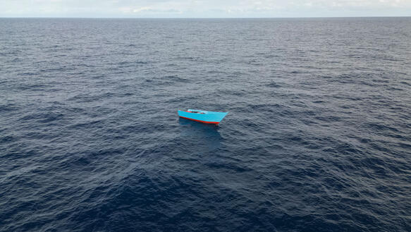 Ein Holzboot treibt mitten im Meer.