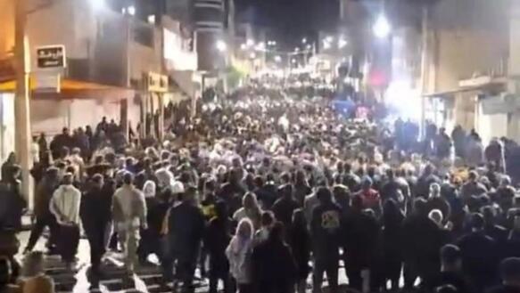 Das Foto zeigt einen großen Demonstrationszug, der nachts durch die beleuchtete Straße in einer Stadt zieht.