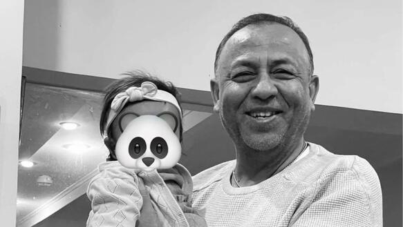 Das Foto zeigt Sylvain Rabetsaroana, der ein kleines Kind auf dem Arm trägt. Er lächelt in die Kamera. Das Foto wurde digital bearbeitet, um das Gesicht des Kindes unkenntlich zu machen. Auf dem Gesicht wurde ein Panda-Gesicht digital platziert.