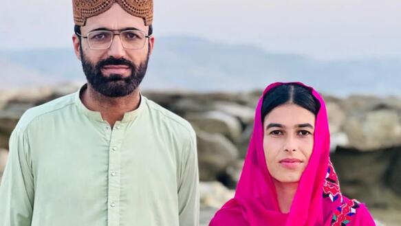 Das Foto zeigt Dad Shah und Fozia Baloc nebeneinander in einer Landschaft stehen und leicht in die Kamera lächelnd. Sie tragen traditionelle Kleidung.