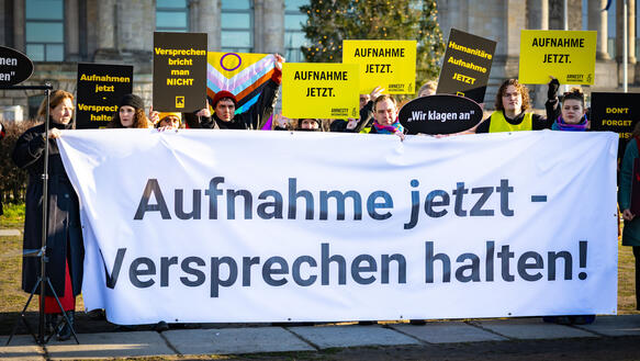 Mehrere Personen protestieren mit Schildern und Papptafeln. Sie halten ein Banner vor sich, auf dem steht: "Aufnahme jetzt – Versprechen halten!"