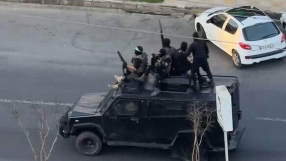 Das Foto zeigt mit Gewehren bewaffnete und maskierte Sicherheitskräfte auf einem Fahrzeug, das durch eine menschenleere Straße fährt.