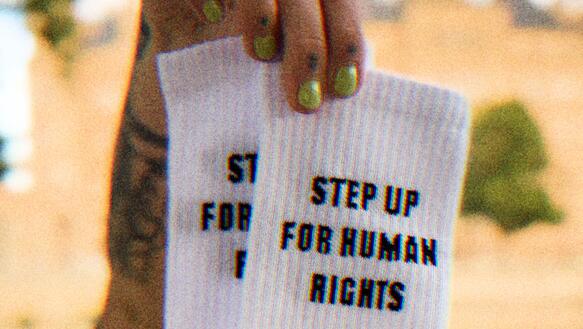 Eine Person hält zwei Socken in der Hand, darauf steht "step up for human rights"