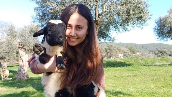Das Foto zeigt Esra Işık auf einer Wiese. Sie hält ein Lamm in den Armen und lächelt in die Kamera.