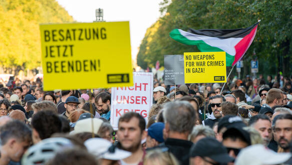 Tausende Menschen demonstrieren auf einer großen, von Bäumen gesäumten Straße. Auf einem Schild mit Amnesty-Logo steht "Besatzung jetzt beenden!"
