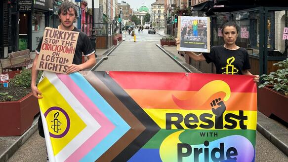 Das Foto zeigt einen jungen Mann und eine junge Frau in einer schmalen Straße. Sie tragen Amnesty-T-Shirts und halten die Intersex-Inclusive-Pride-Flagge vor sich, auf dem steht "Resist with pride". Sie halten außerdem kleine Plakate in der Hand. Auf dem des Mannes steht: "Turkiye, stop the crackdown on LGTBIQ+ rights".