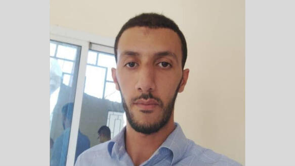 Porträtfoti von Mustapha Dihani, der ein Hemd mit Kragen trägt und ernst in die Kamera blickt.