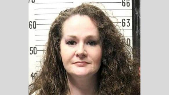 Polizeiaufnahme (Mugshot) von Christa Pike. Frontale Porträtaufnahme vor einer Wand mit genauer Größentabelle im Hintergrund.