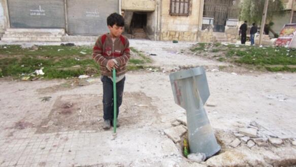 Ein Kind steht neben einer Streubombe, die am 01. März 2013 über Aleppo abgeworfen wurde