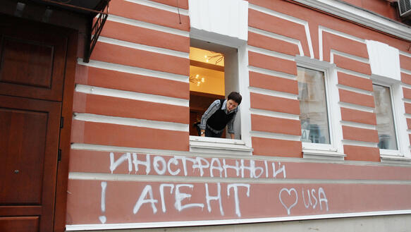 Eine Person sieht aus dem Fenster eines Gebäudes, auf das ein kyrillischer Schriftzug gesprüht wurde.