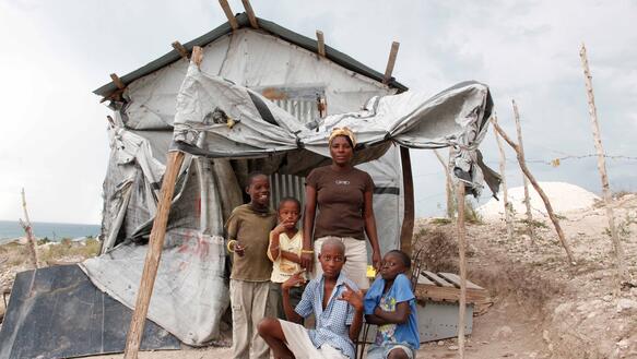 Eine Frau steht mit vier Kindern vor einem brüchigen Haus