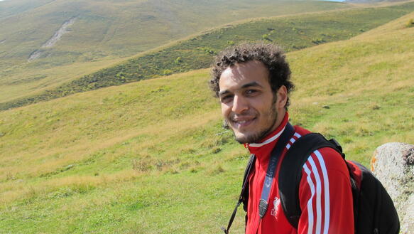 Porträtfoto eines Mannes in einer grünen, hügeligen Landschaft