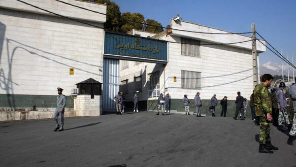 Mehrere Polizisten und Sicherheitsbeamte in unterschiedlichen Uniformen stehen verstreut auf einem asphaltierten Platz vor einem Gefängnistor