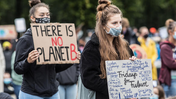 Zwei junge Frauen mit Mundschutz halten Plakate hoch.