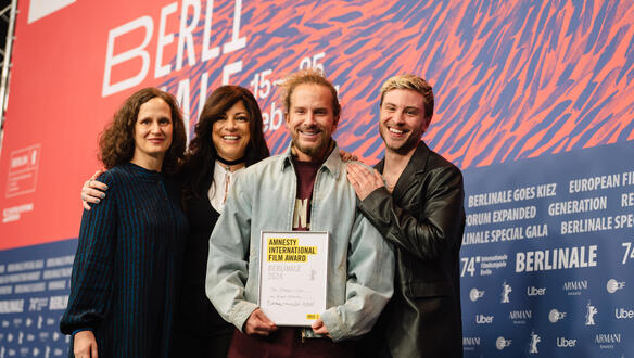 Gruppenfoto der drei Jury-Mitglieder und dem Regisseur, der eine Urkunde in der Hand hält. Die vier Personen stehen nebeneinander und lächeln.