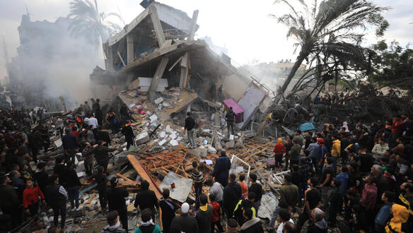 Das Bild zeigt eine Menschenmenge vor einem zerstörten Gebäude
