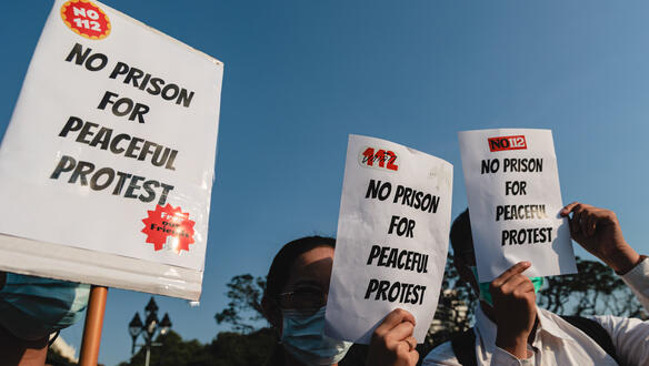 Das Foto zeigt drei Personen bei einer Demonstration. Sie halten Schilder hoch, auf denen steht: "No prison for peaceful protest".