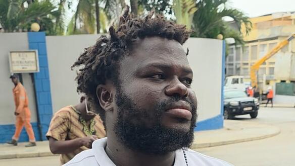 Aufnahme von Serrote José de Oliveira auf einer Straße. Er hält die Hände verschränkt vor seinen Bauch und blick ernst seitlich an der Kamera vorbei.