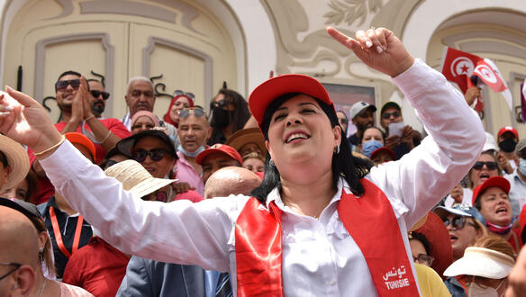 Das Foto zeigt Abir Moussi inmitten einer Menschenmenge. Sie lacht und trägt eine Schirmmütze und einen Schal mit der Aufschirft "Tunisie".