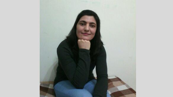 Porträtfoto von Zeynab Jalalian, die ihr Kinn auf ihre rechte geschlossene Hand stützt und ernst in die Kamera blickt.